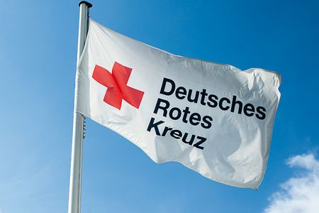 DRK Flagge Im Wind weht eine weiße Flagge. Sie zeigt ein rotes Kreuz. Daneben steht in schwarzen Buchstaben: Deutsches Rotes Kreuz.